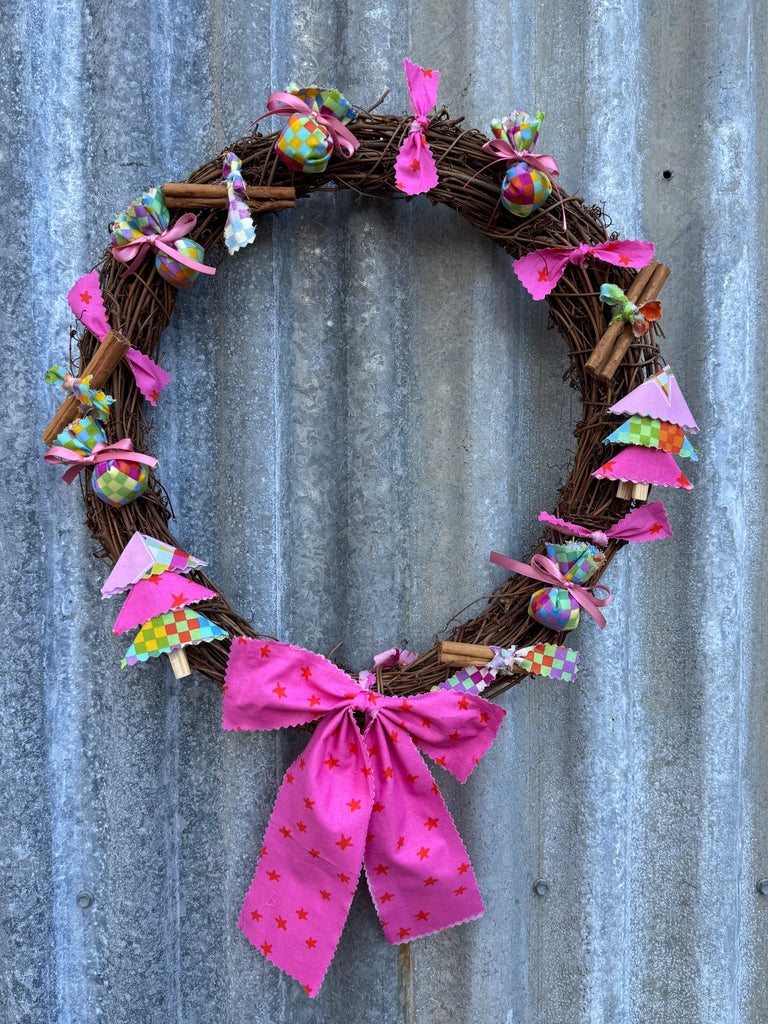Decorative wreath with pink ribbon and small ornaments on a metallic surface