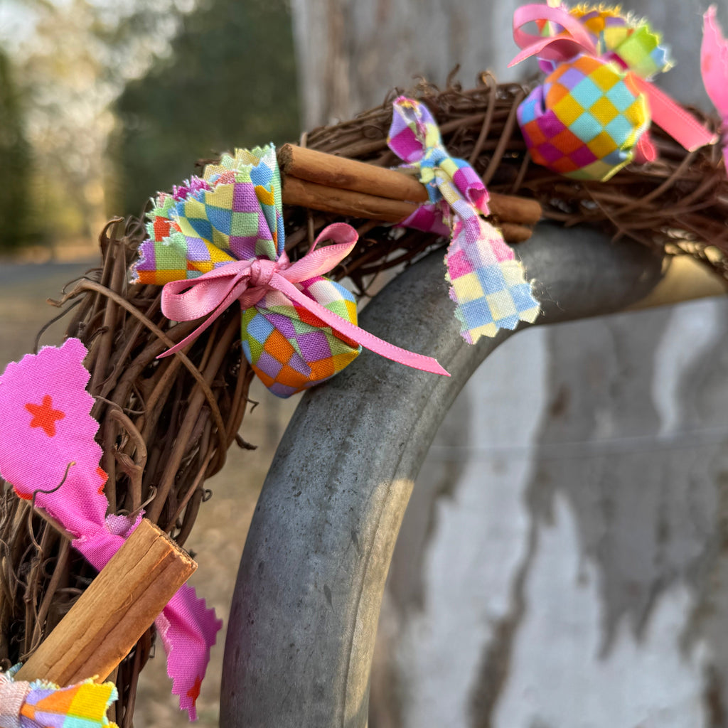 Close up of decorative wreath with colourful balls and ribbons on a metal surface.