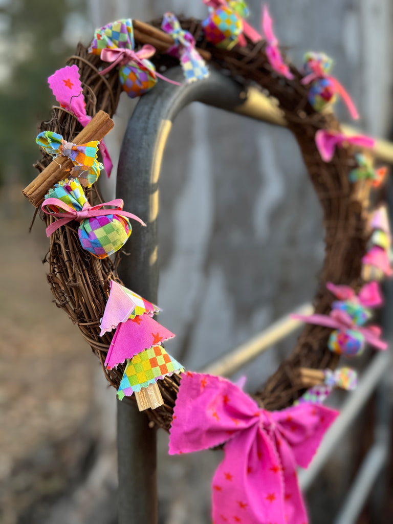 Side angle of decorative wreath with colourful ribbons and a cross, hanging on a metal gate.